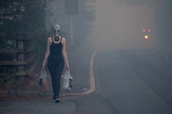 Người phụ nữ đeo mặt nạ chống khói đi chợ sau một đám cháy rừng