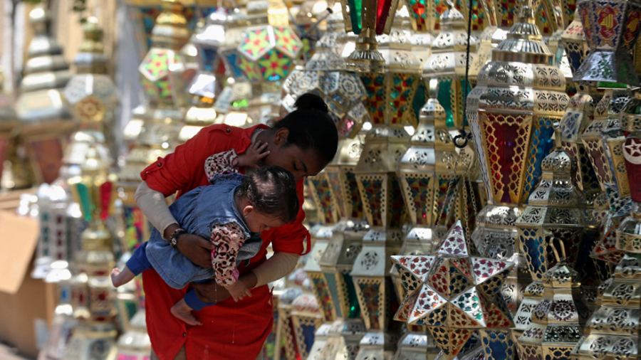 Một phụ nữ Ai Cập bế con đi dạo bên cạnh quầy hàng bán đèn lồng Ramadan truyền thống ở thủ đô Cairo ngày 12/4