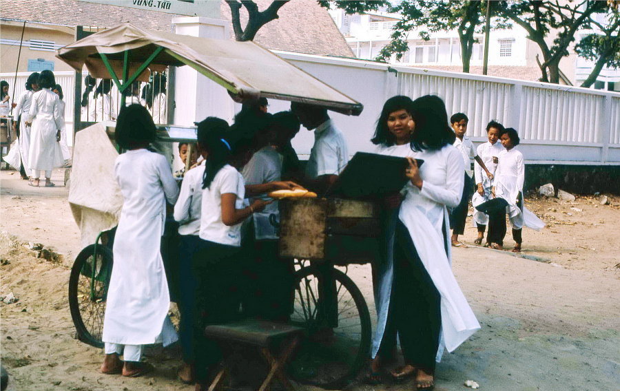 Các nữ sinh tụ tập bên quầy bánh mì bên ngoài cổng trường học