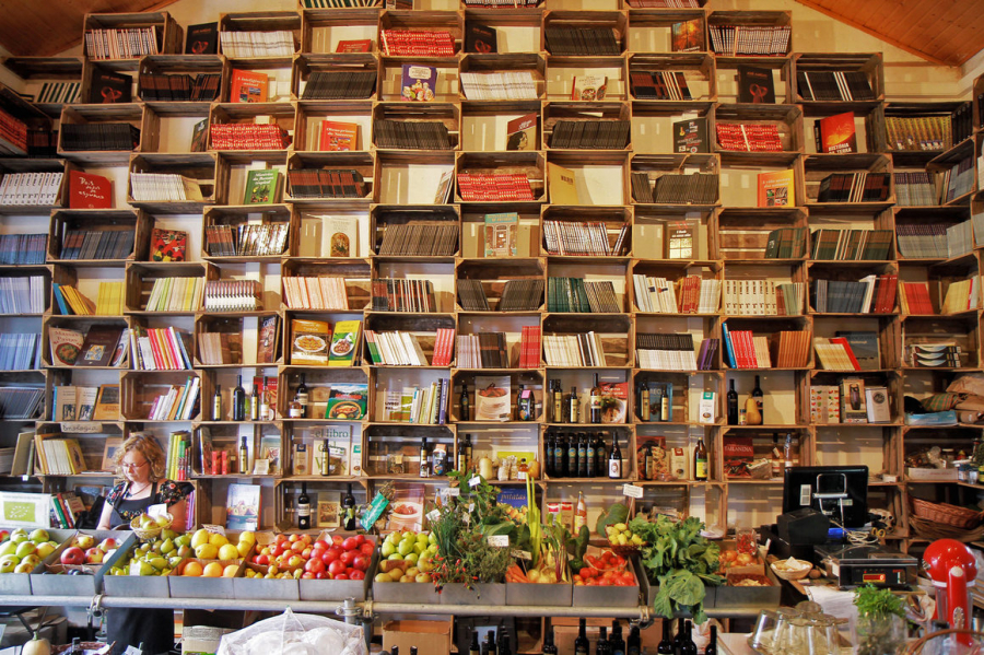 Một  tiệm tạp hóa có kệ sách nấu ăn đằng sau quầy trái cây tươi và rau quả