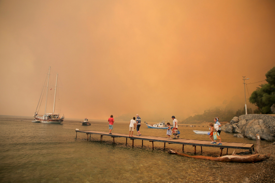 Khách du lịch chờ sơ tán khi đám cháy lan tràn xuống đồi về phía bờ biển Bodrum, Thổ Nhĩ Kỳ. Trên khắp đất nước, du khách không còn lựa chọn nào khác ngoài việc rời bỏ những bãi biển du lịch xinh đẹp một thời. (Ảnh: Emre Tazegul/Associated Press)