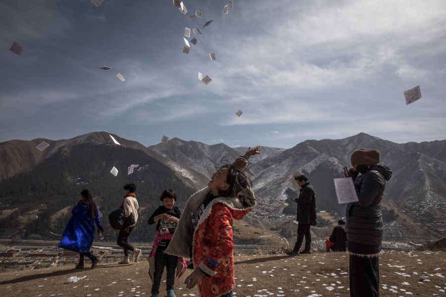 Một cô gái ném những tờ giấy tượng trưng cho sự may mắn trên một ngọn đồi nhìn ra tu viện Labrang trong kỳ Monlam.  