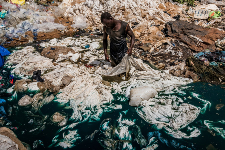 Một người đàn ông rửa túi nhựa trong bãi rác ở vùng đầm lầy, nơi thuốc nhuộm màu xanh từ nhựa đã ngấm vào nước hồ ở Uganda. (Ảnh: Frédéric Noy)